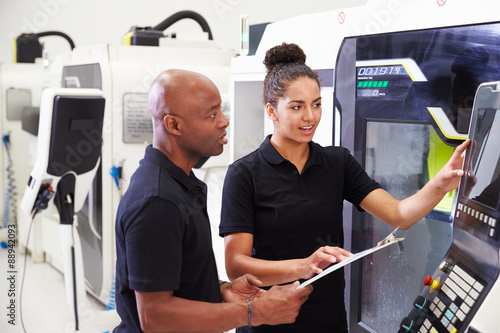 Female Apprentice Working With Engineer On CNC Machinery