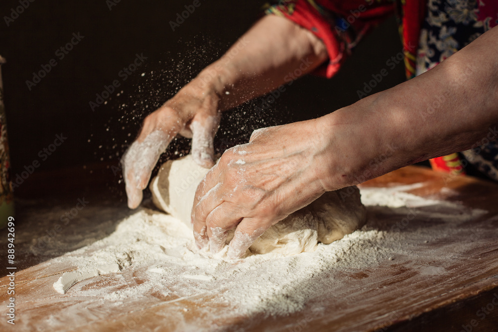 Fototapeta premium Senior woman hands knead dough on a table in her home kitchen