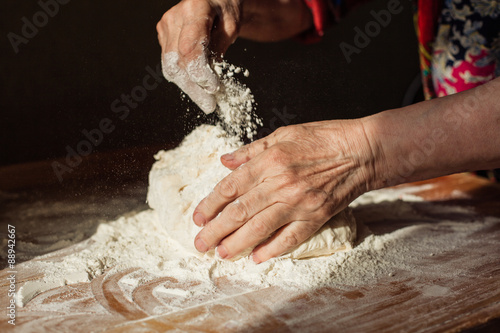 Senior woman hands knead dough on a table in her home kitchen photo