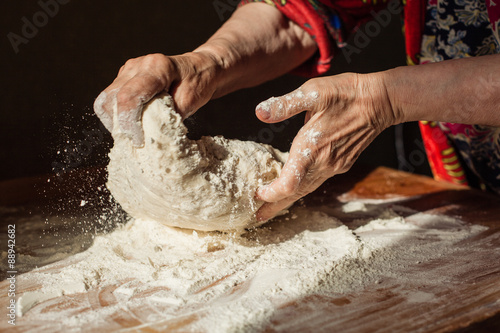 Fotografi Senior woman hands knead dough on a table in her home kitchen