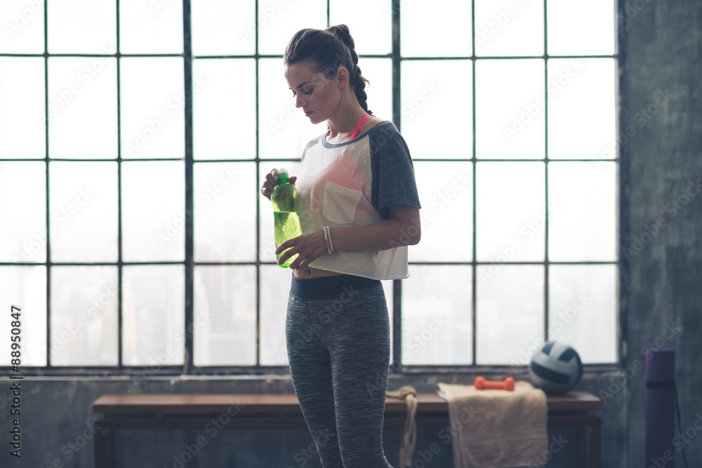 Fit woman standing in profile in loft gym holding water bottle