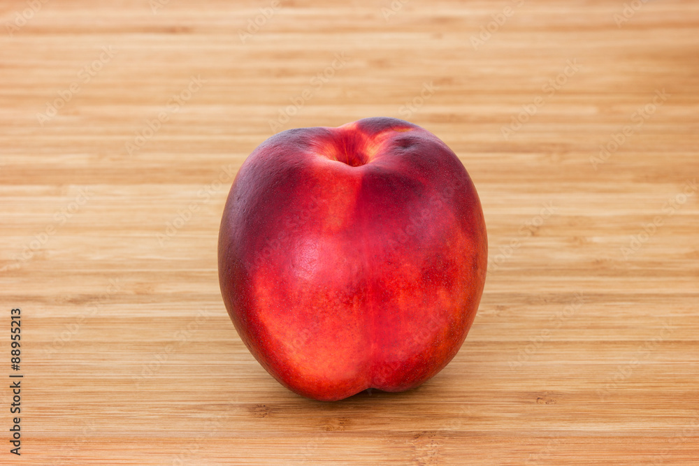 Close-up of a whole ripe nectarine/peach (Prunus persica) on a wooden chopping board. Close-up of a whole ripe nectarine/peach (Prunus persica) on a wooden chopping board.