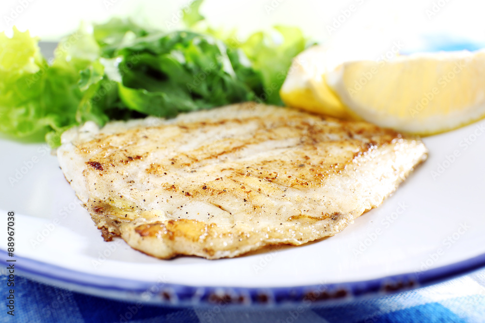 Dish of fish fillet with lettuce and lemon on table close up Dish of fish fillet with lettuce and lemon on table close up