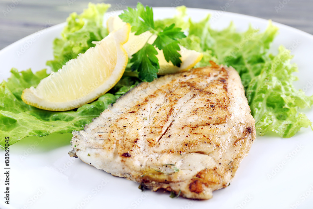 Dish of fish fillet with lettuce and lemon on plate close up