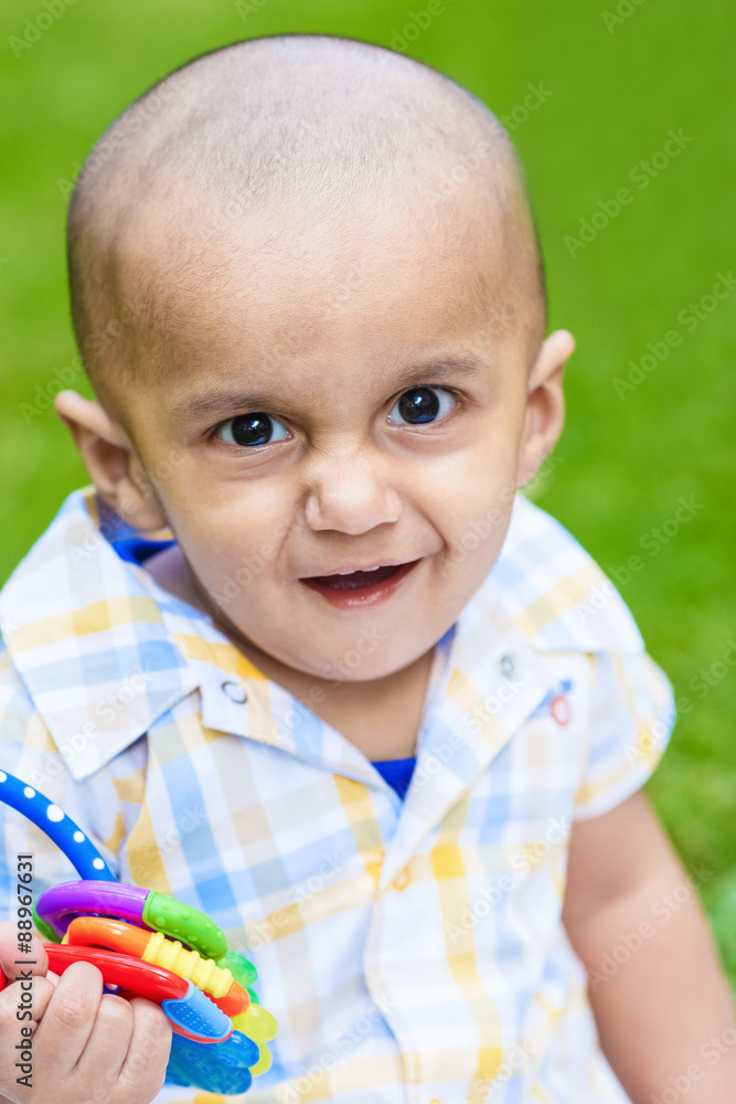 Portrait of cute adorable smiling laughing little indian mixed race infant  boy with funny hilarious face expression in plaid shirt on green grass park  background playing with toy Stock Photo | Adobe