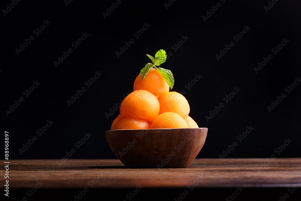 Organic cantaloupe melon in wooden bowl isolated on black backgr