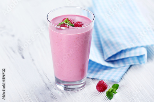 Glass of raspberry milk shake with berries on wooden table close up