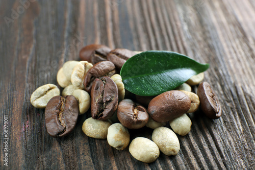 Green and brown coffee beans with leaf on wooden background