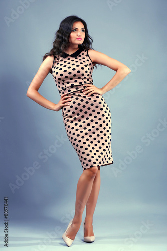 Portrait of young pretty woman in beige dots dress on grey background © Africa Studio
