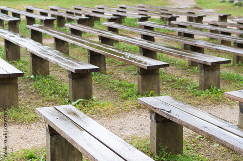 Wet wooden benches after rain in park, outdoor stage area