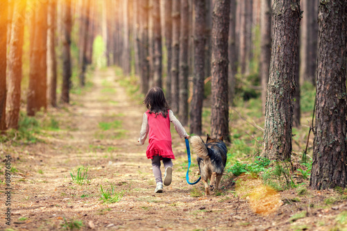 Little girl walking with big dog in the pine forest