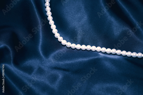 white pearl necklace on a dark blue silk
