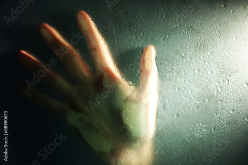 Female hand behind  wet glass  close-up