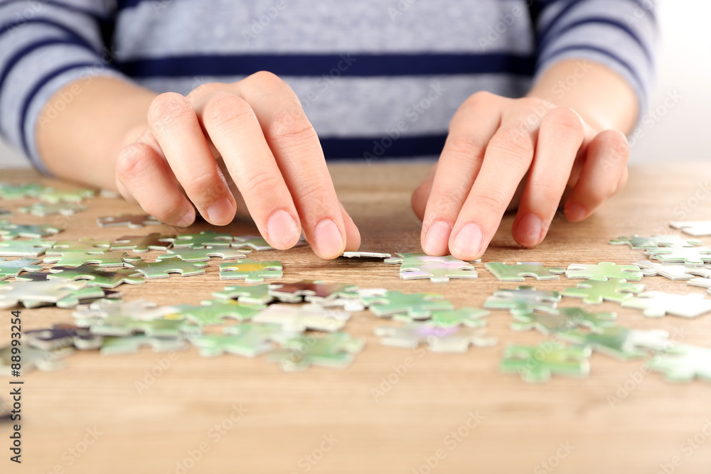 Female hands assembling puzzle on wooden table, closeup Female hands assembling puzzle on wooden table, closeup