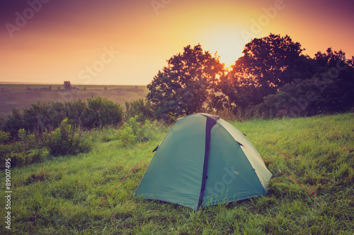 Tourist tent on green meadow at sunrise. Camping background. Freedom concept.