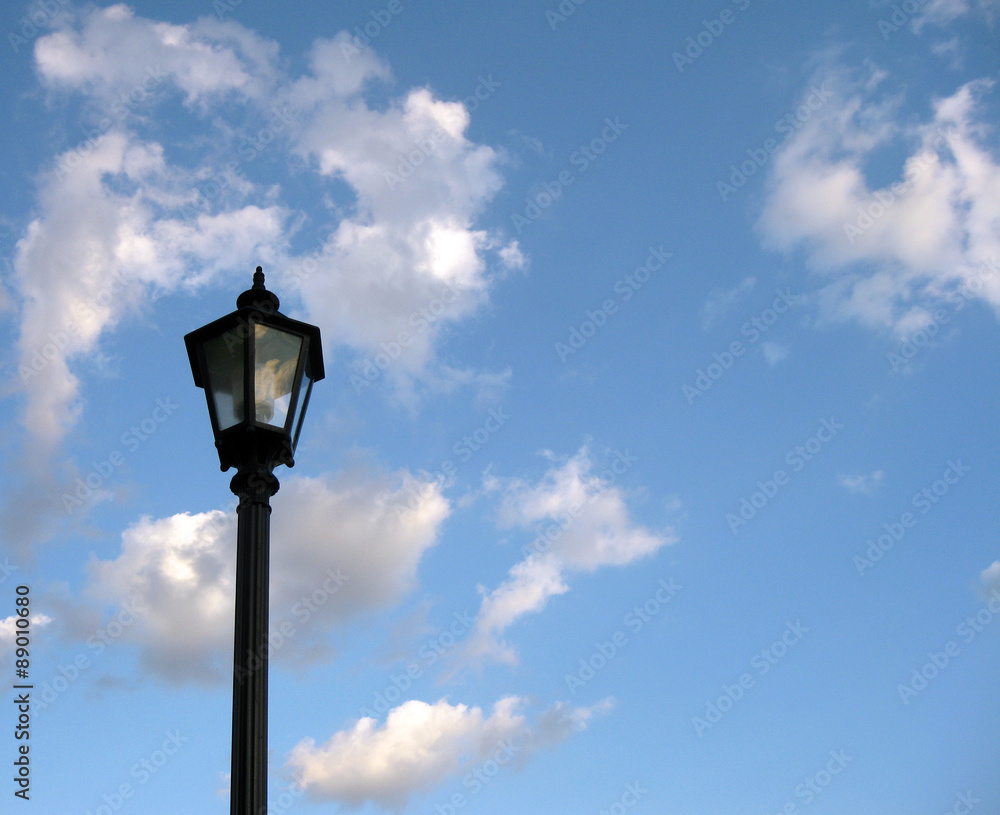 An old-fashioned streetlight against a cloudy, blue, summer sky. Space for text.