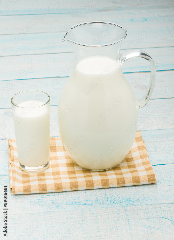 A glass of milk and a milk jug on plaid tablecloth. A glass of milk and a milk jug on plaid tablecloth.