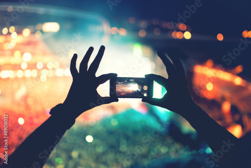 Silhouette of hands using camera phone to take pictures and videos at pop concert, festival. Soft effect on photo