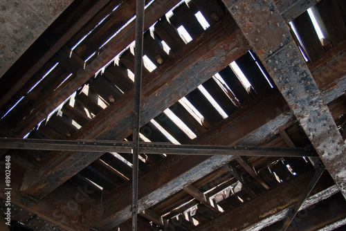 Underside of old railroad bridge showing rusty steel girders and train tracks