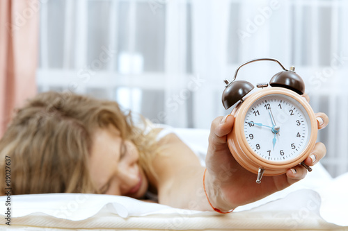 Young woman with alarmclock on the bed.