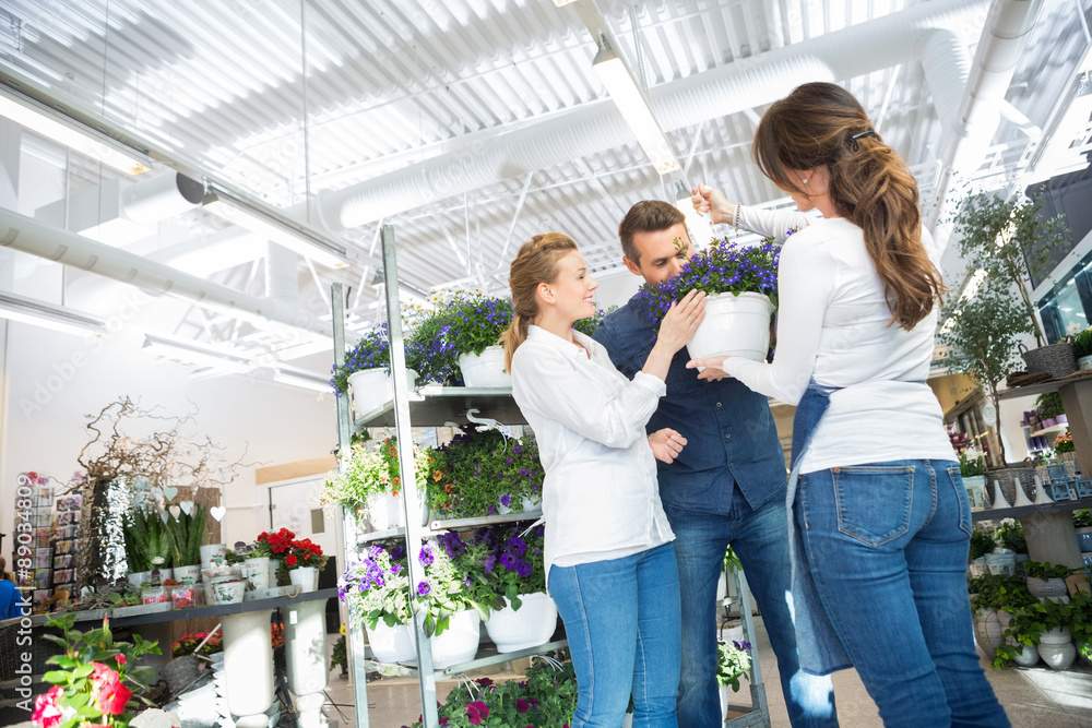 Female Florist Guiding Couple In Buying Purple Flower Plant