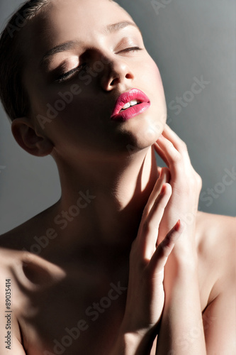 Young emotional girl with pink lips posing in front of grey