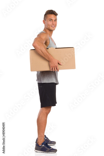 Muscular Man Holding Carton Box Under His Arm. Side view. Full length studio shot isolated on white. © studioloco