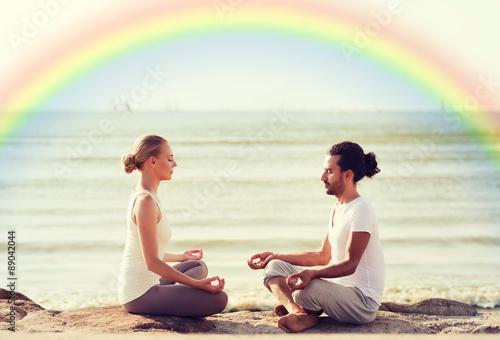 happy couple meditating in lotus pose on beach