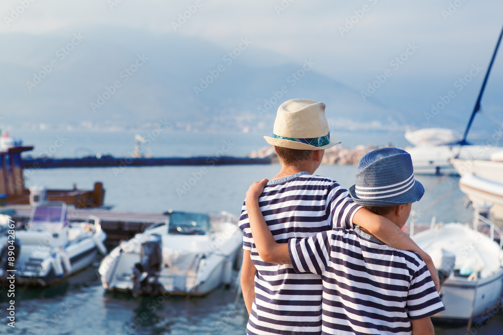 Two brothers hug and look at ships, yacht at sea