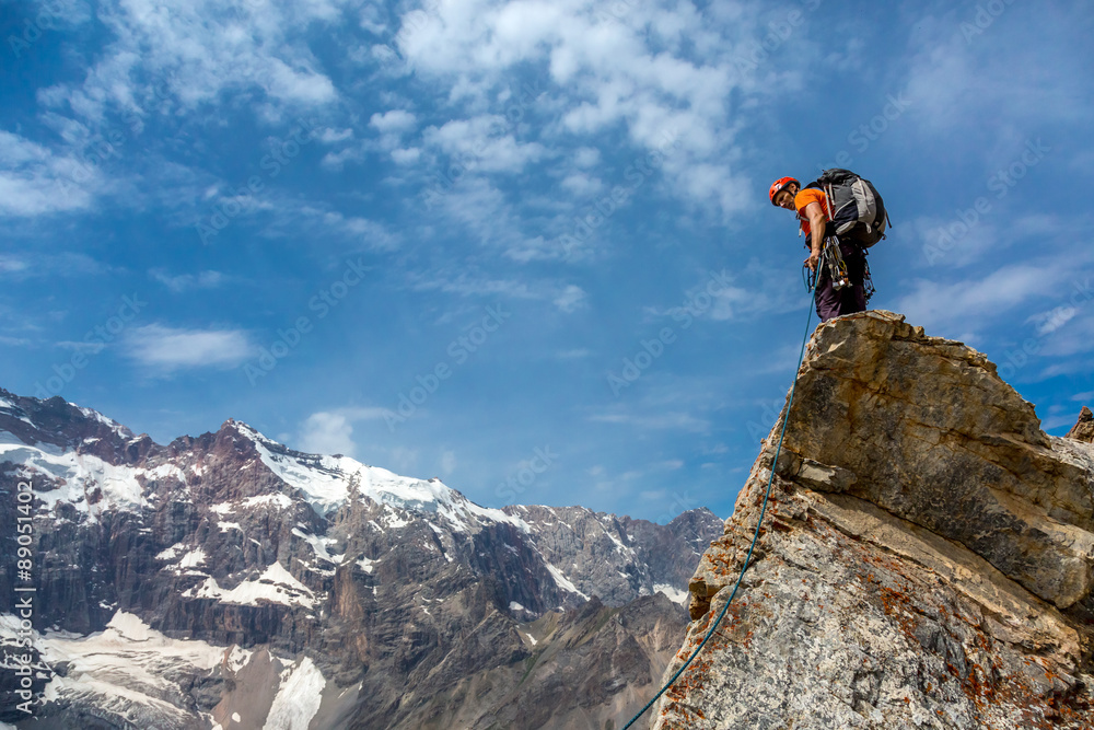 Mountain climber on top Rocky razor sharp pointed summit and silhouette of male climber staying on sky and remote high land ridge background daylight sunny day outdoors