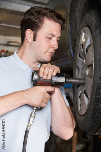 Mechanic In Garage Using Air Hammer On Car Wheel