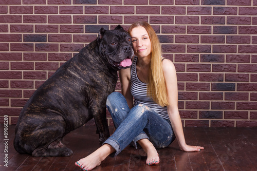 girl sitting near brick wall next to the dog Cane Corso