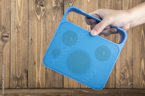 Man's Hand Carrying Blue Handy Speaker on Wooden Background