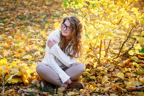beautiful woman in glasses sitting on yellow leaves