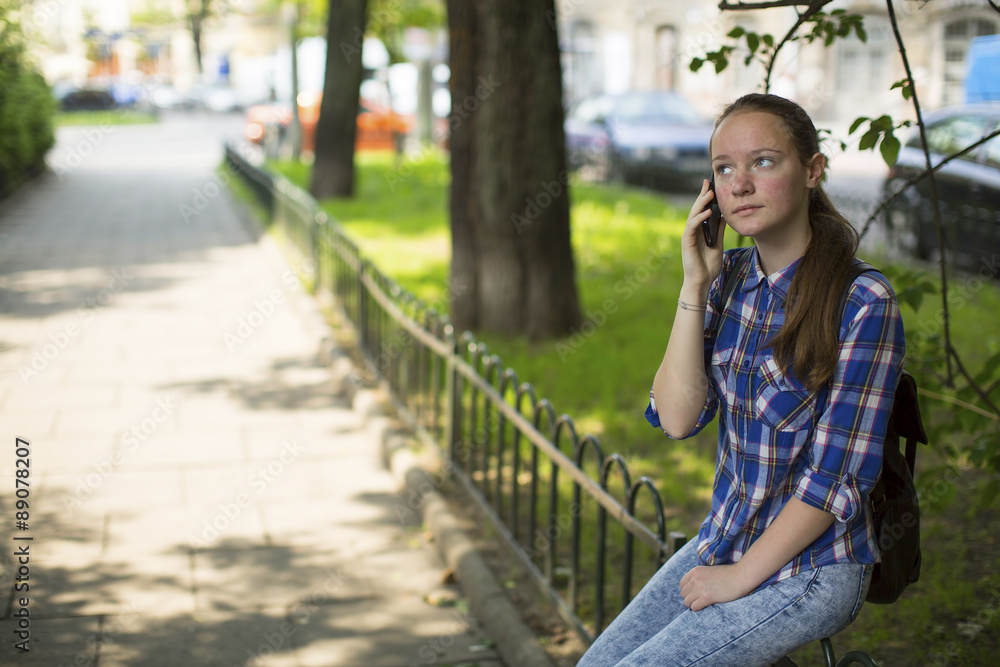 Teenage girl anxiously talking on the cell phone while sitting outdoors. Teenage girl anxiously talking on the cell phone while sitting outdoors.