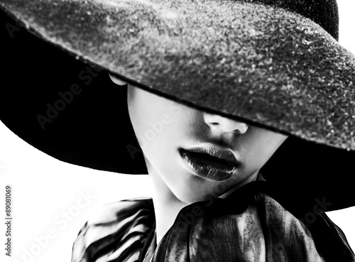 Beautiful woman with full lips in black hat poses on white