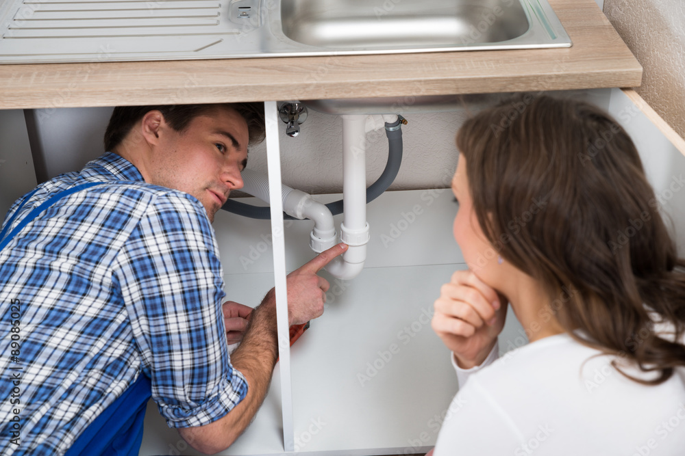 Plumber Showing Damage In Sink Pipe To Woman Plumber Showing Damage In Sink Pipe To Woman