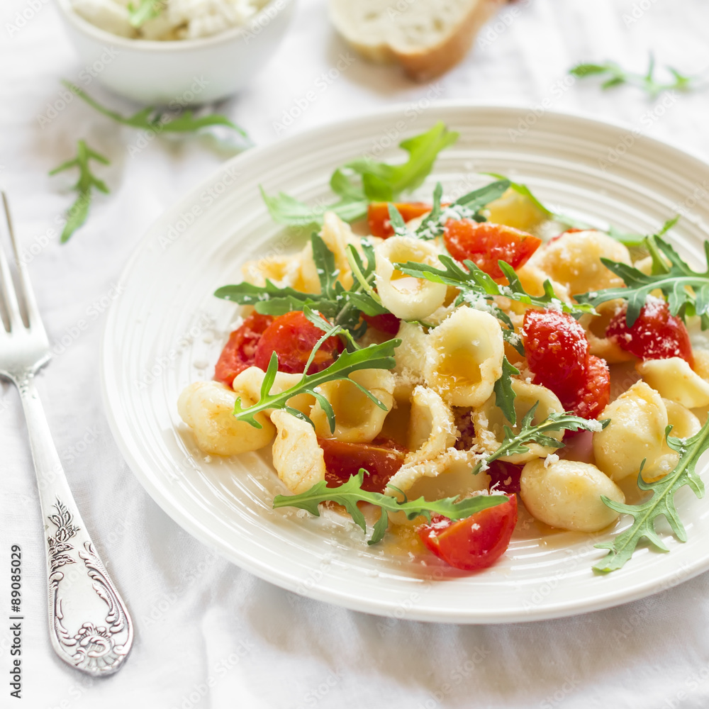 orecchiette pasta with cherry tomatoes, arugula and Parmesan cheese on a white plate on a light background