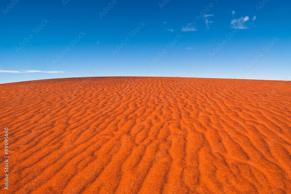 A rippled red sand dune against a clear blue sky, taken near Uluru