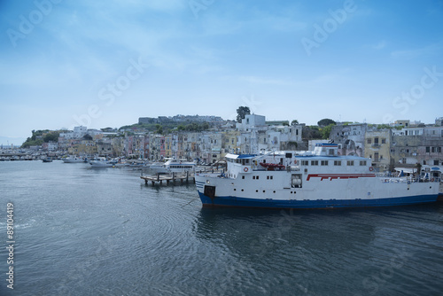 Island of Procida view from the boat. Coast line, port, ships and boats, curtain of houses in a row, bright colors and typical village. blue sky.