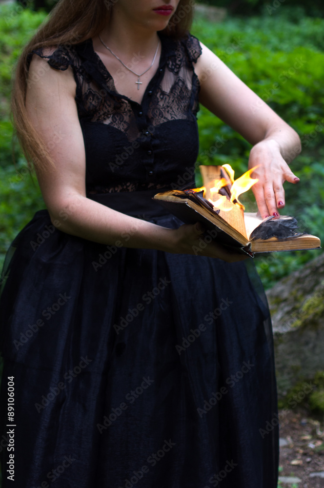 A woman in a black dress holds black burning book
