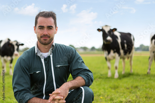 Fotografiet Portrait of a young attractive farmer in a pasture with cows