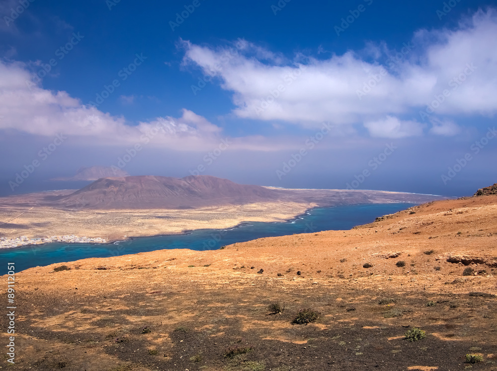 View of the La Graciosa island from a slope of Mount Mirador del Rio on background blue sky and Atlantic Ocean. Lanzarote, Canary Islands, Spain View of the La Graciosa island from a slope of Mount Mirador del Rio on background blue sky and Atlantic Ocean. Lanzarote, Canary Islands, Spain