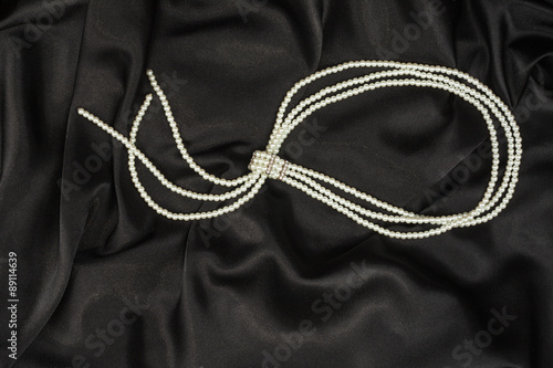 White elegant beads lie on the black silk