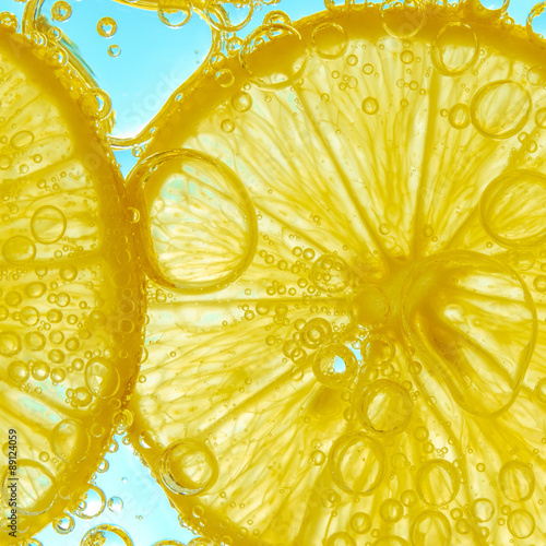 Fresh lemon slice in water with bubbles on sky background