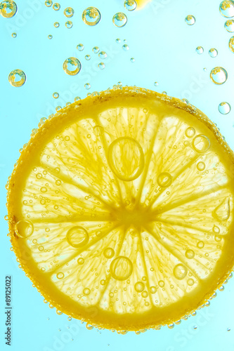 Fresh lemon slice in water with bubbles on sky background