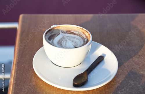 The coffee cup with a picture and a chocolate spoon on the table in the cafe