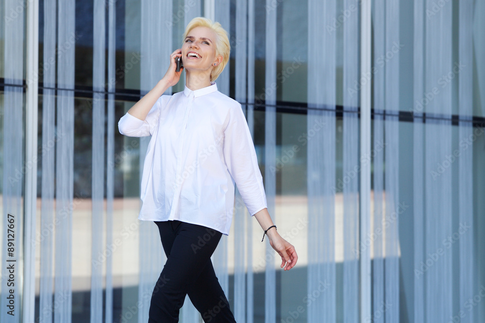 Obraz premium Young woman smiling and walking with mobile phone