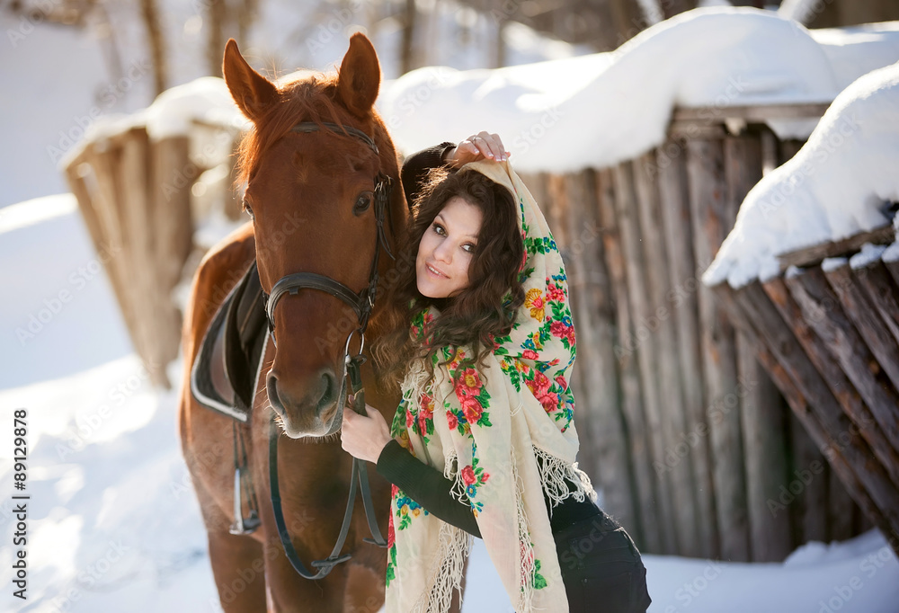 beautiful young woman in Russian national scarf with a horse in the countryside in winter