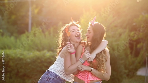 Cheerful friends walking in a summer park. Girls lick lollipops. The concept of true friendship.